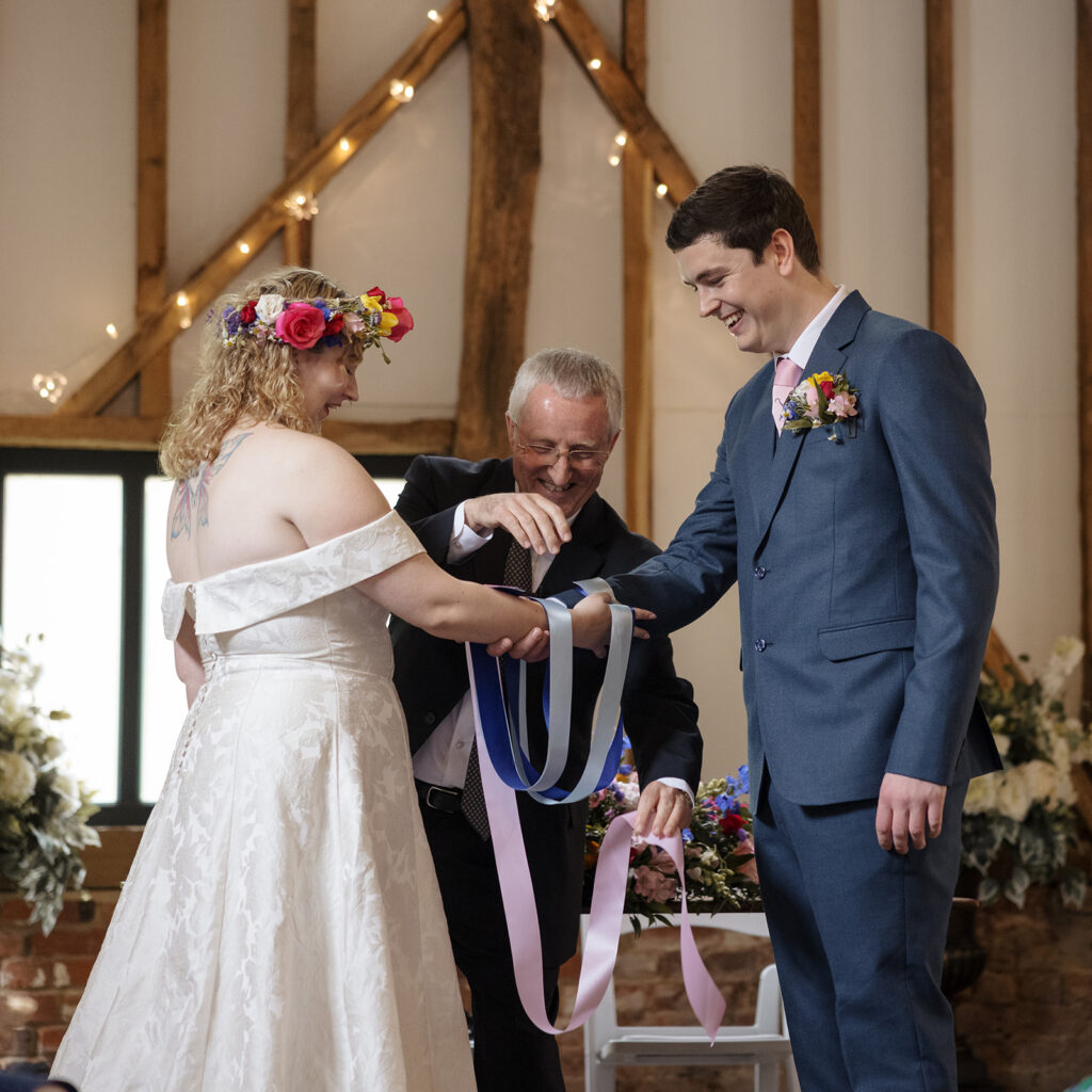 A Civil Weddings handfasting ritual held in Essex barn beneath timber beams and fairy lights.