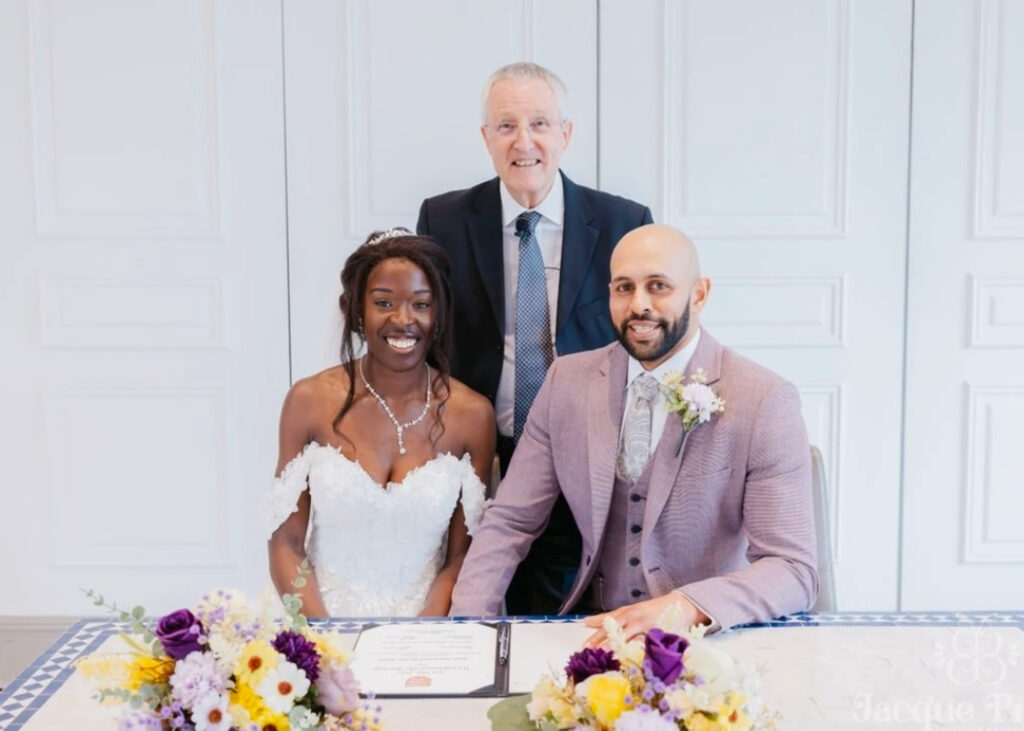 Newly married couple signing their wedding certificate with the celebrant standing behind them.