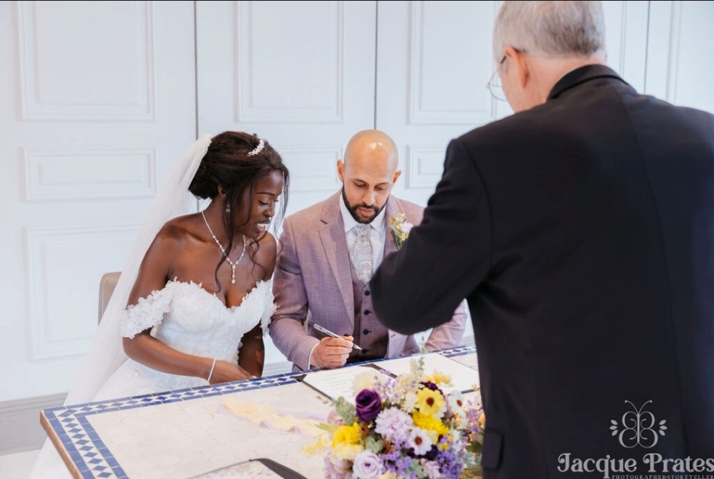 Couple signing their ceremony certificate at a table, with the officiant overseeing the moment
