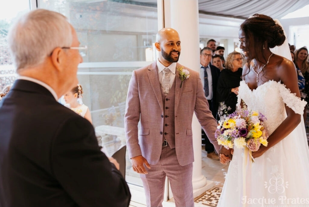 Bride entering the indoor ceremony space with her colourful bouquet, welcomed by smiling guests
