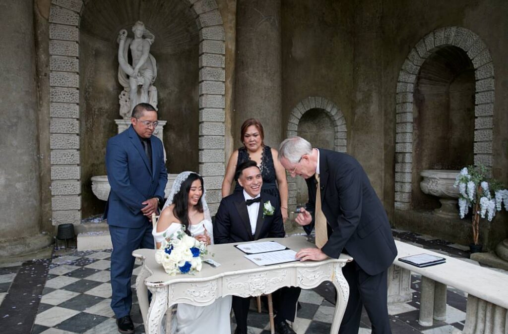 Bride and groom seated together as their celebrant signs their certificate at Wotton Hall.